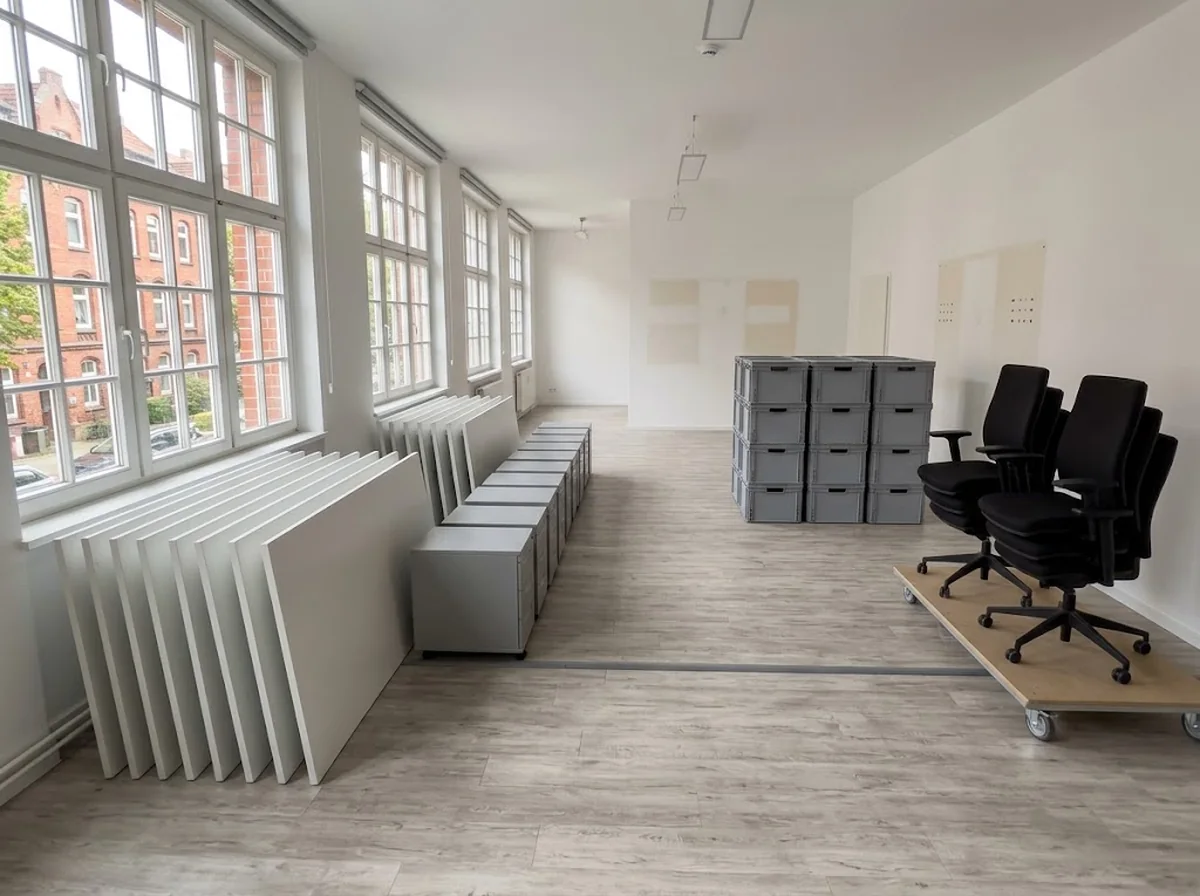 Dasselbe Büro geräumt, Tischplatten aufgereiht an der Wand, Stühle und Container abholbereit